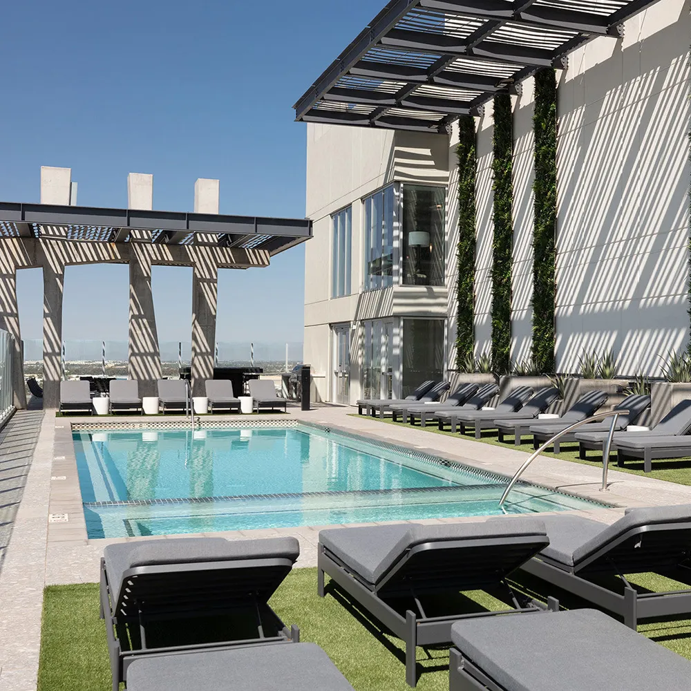 Modern rooftop pool with gray lounge chairs, glass railings, and vertical garden on white wall.