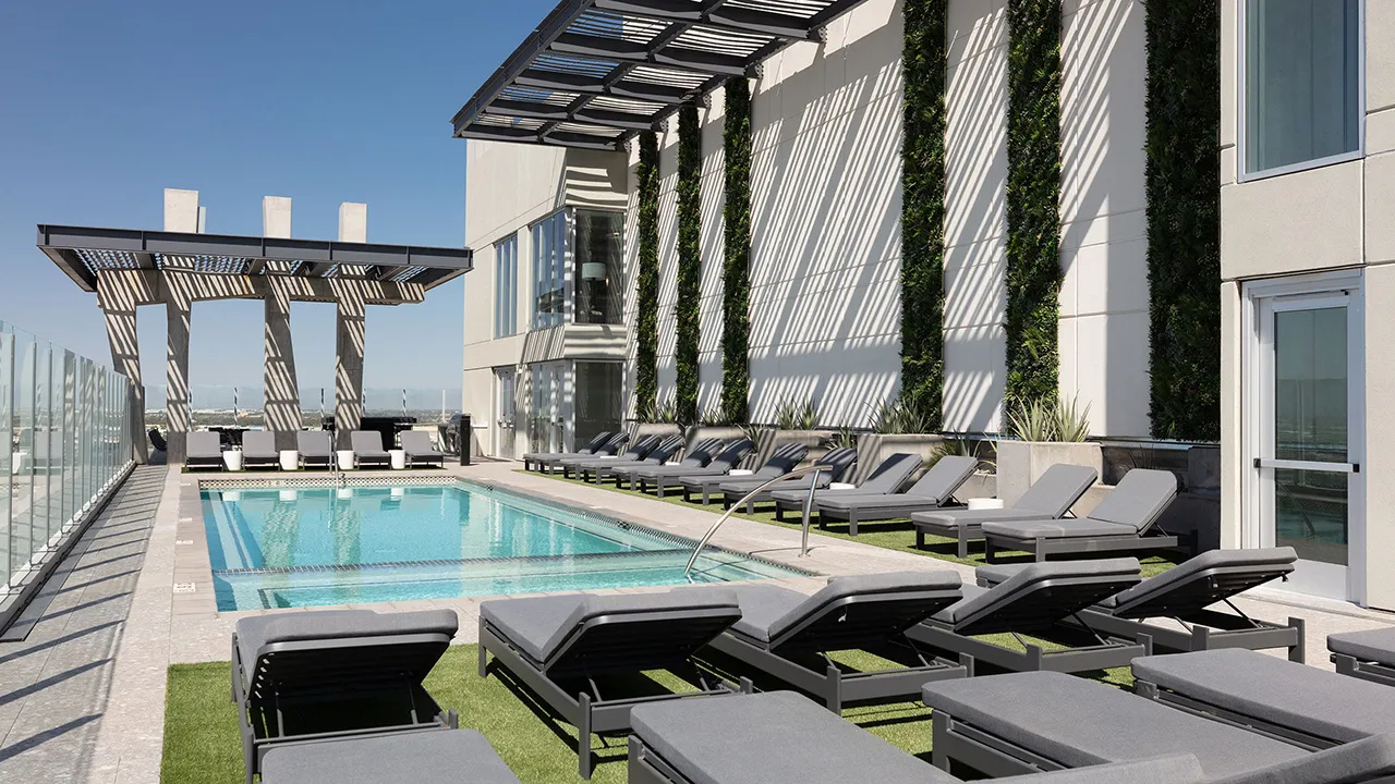 Modern rooftop pool with gray lounge chairs, glass railings, and vertical garden on white wall.
