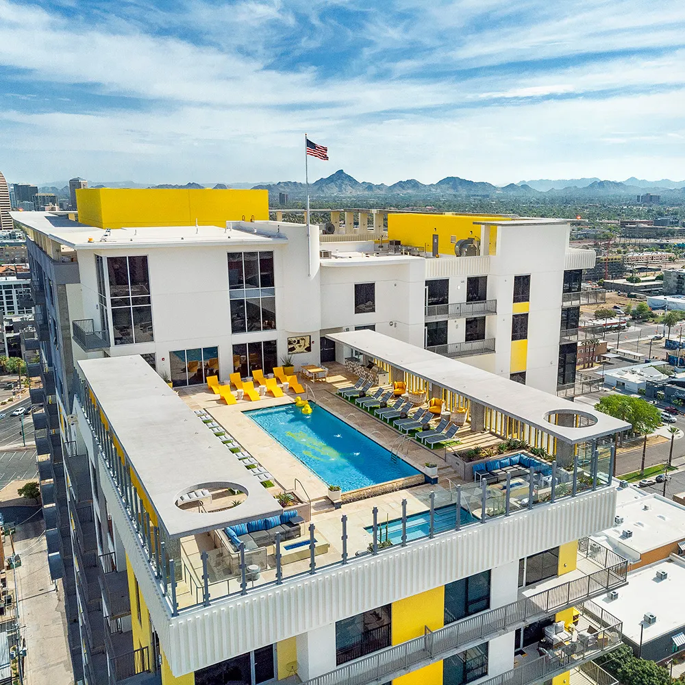 Aerial view of a rooftop pool with yellow lounge chairs and cityscape with mountains in the background.