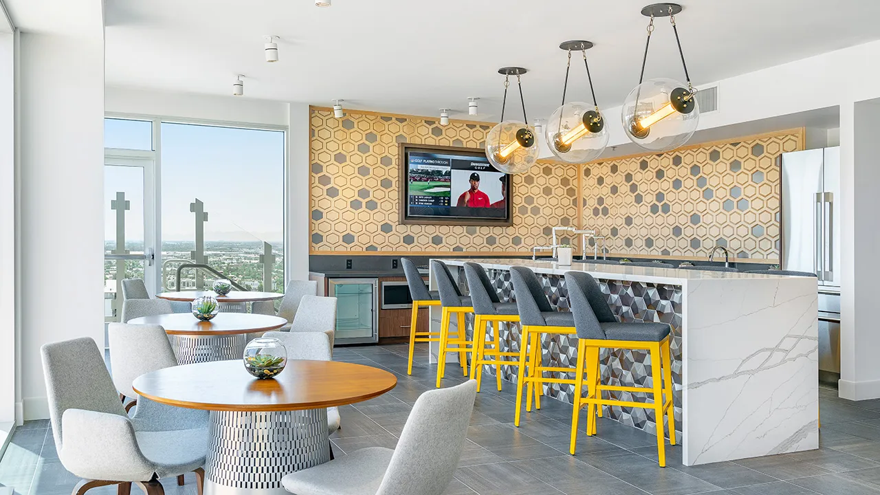 Modern clubhouse interior with round tables, gray chairs, yellow bar stools, and hexagonal wall tiles.