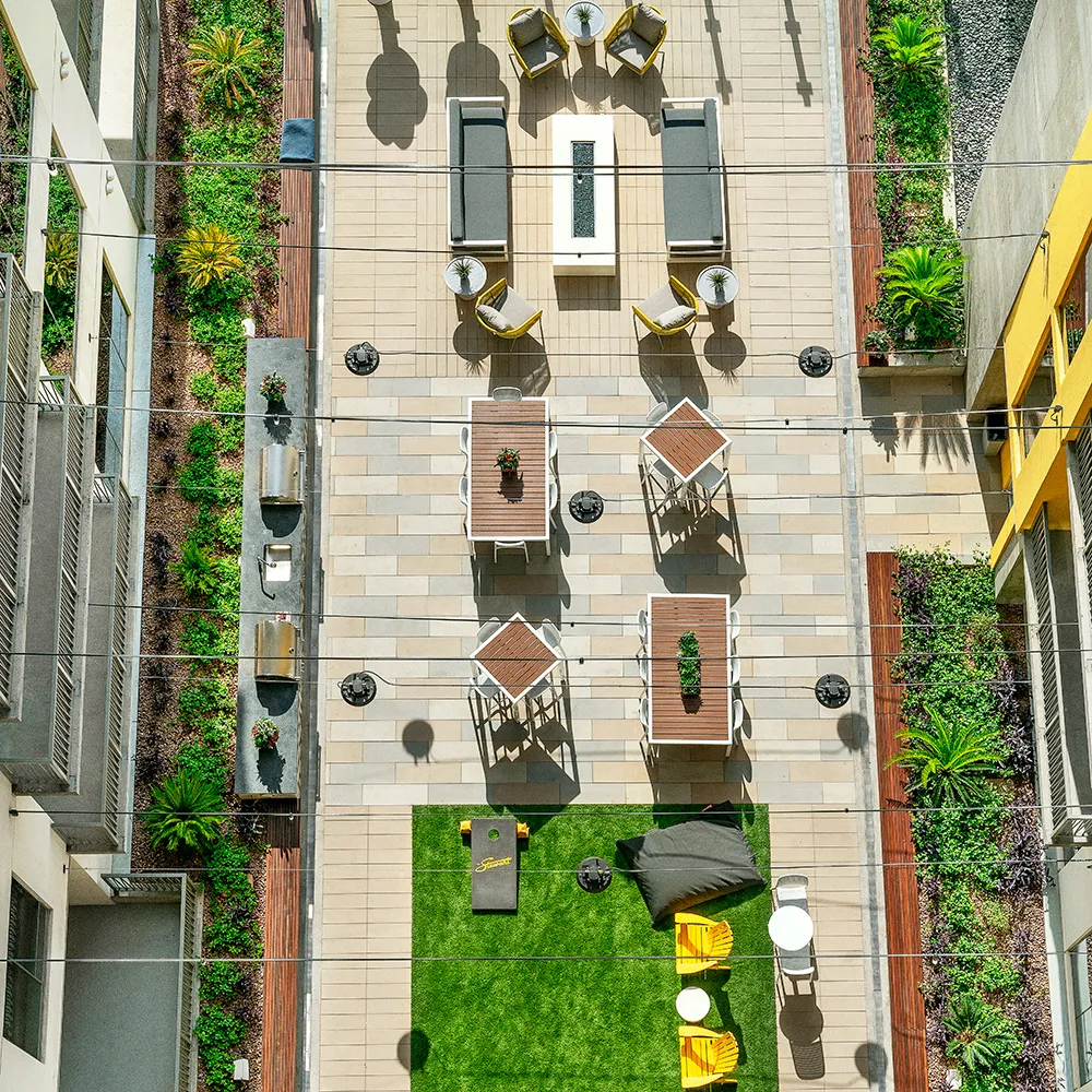Bird's-eye view of a courtyard with outdoor seating, tables, grills, and green landscaping.