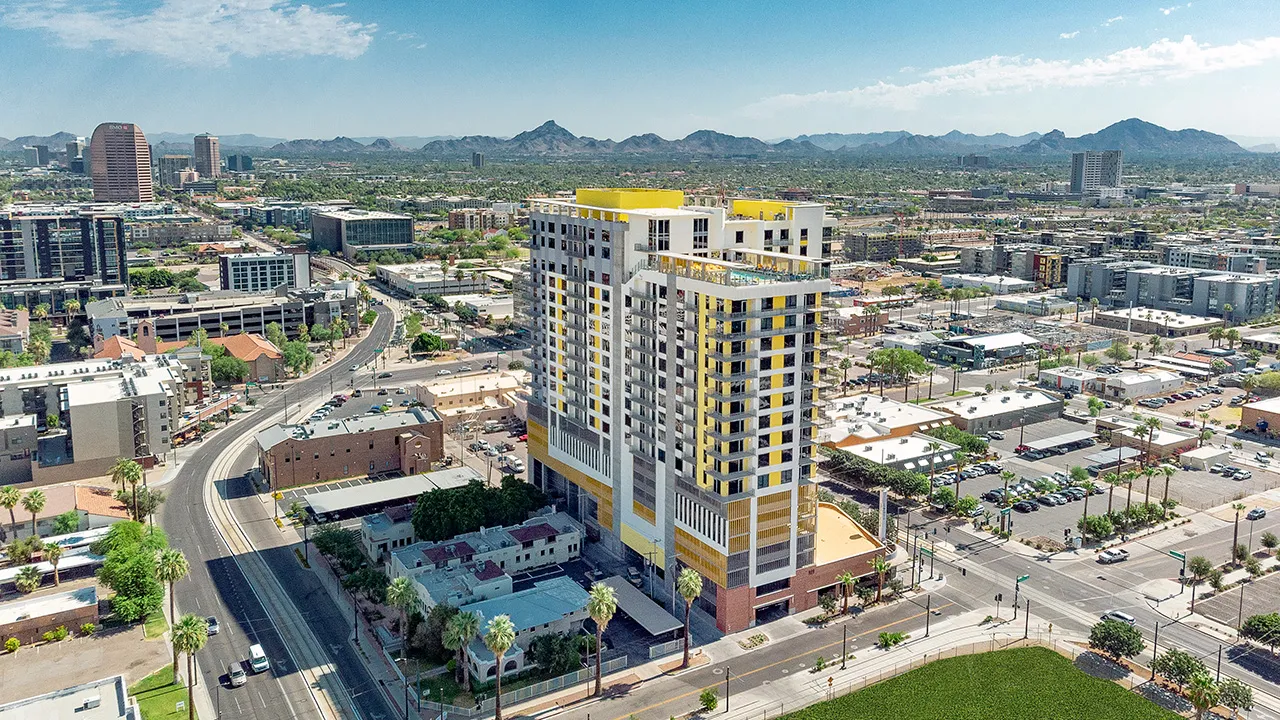 The Stewart, a high-rise residential building with balconies overlooking a city street and skyline under clear blue sky.