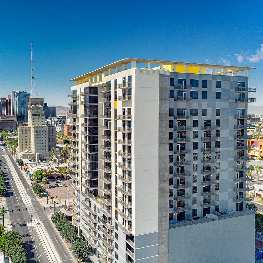 The Stewart, a high-rise residential building with balconies overlooking a city street and skyline under clear blue sky.