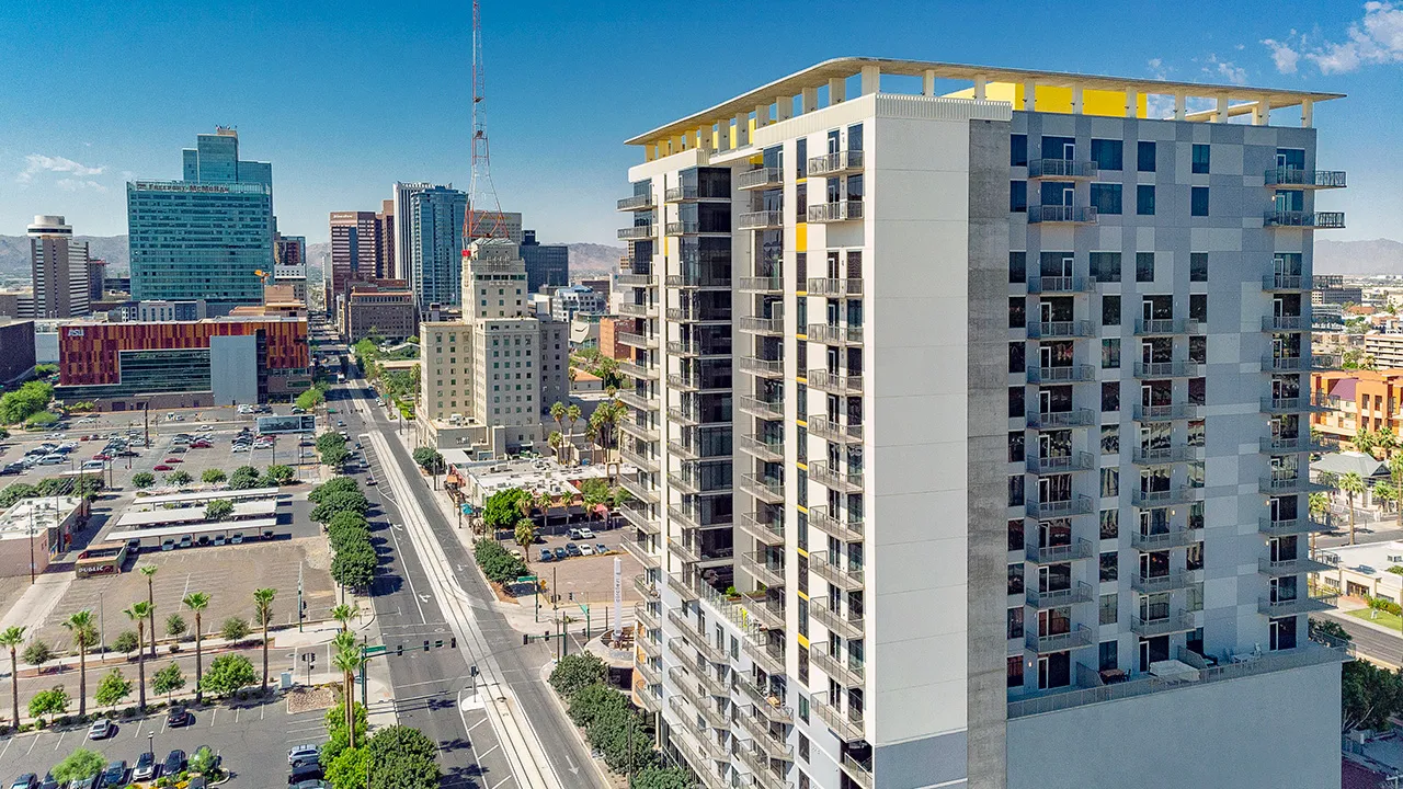 The Stewart, a high-rise residential building with balconies overlooking a city street and skyline under clear blue sky.
