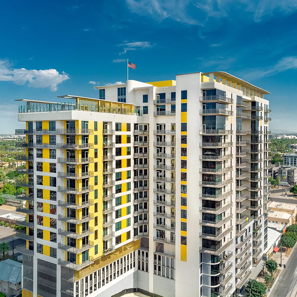 The Stewart, a modern multi-story building with yellow accents and balconies under a partly cloudy sky.