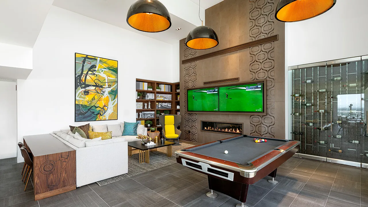 Modern game room with pool table, sectional sofa, abstract wall art, and dual TVs above a fireplace.