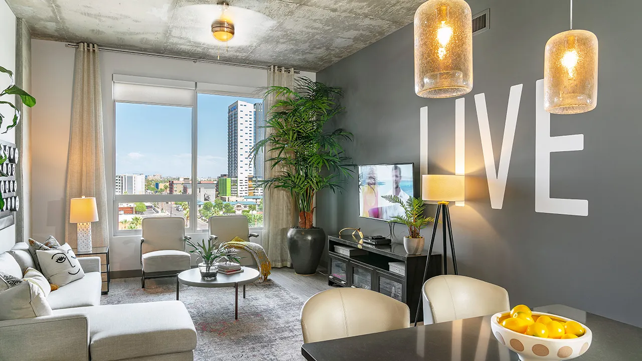 Modern living room with large window, gray walls, white sofa, plants, TV, and hanging lights.