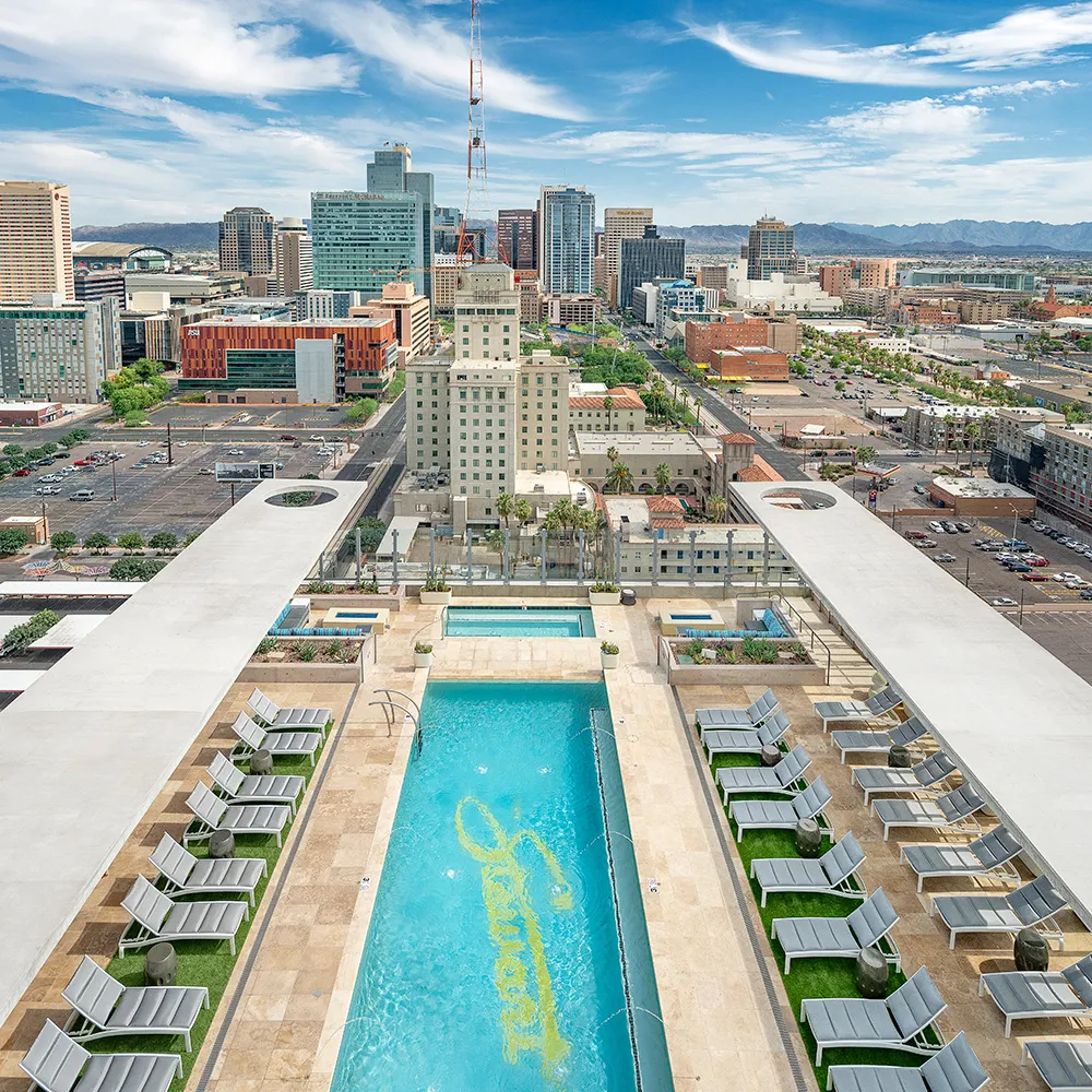 Rooftop pool with lounge chairs overlooking a city skyline with buildings and mountains in the distance.