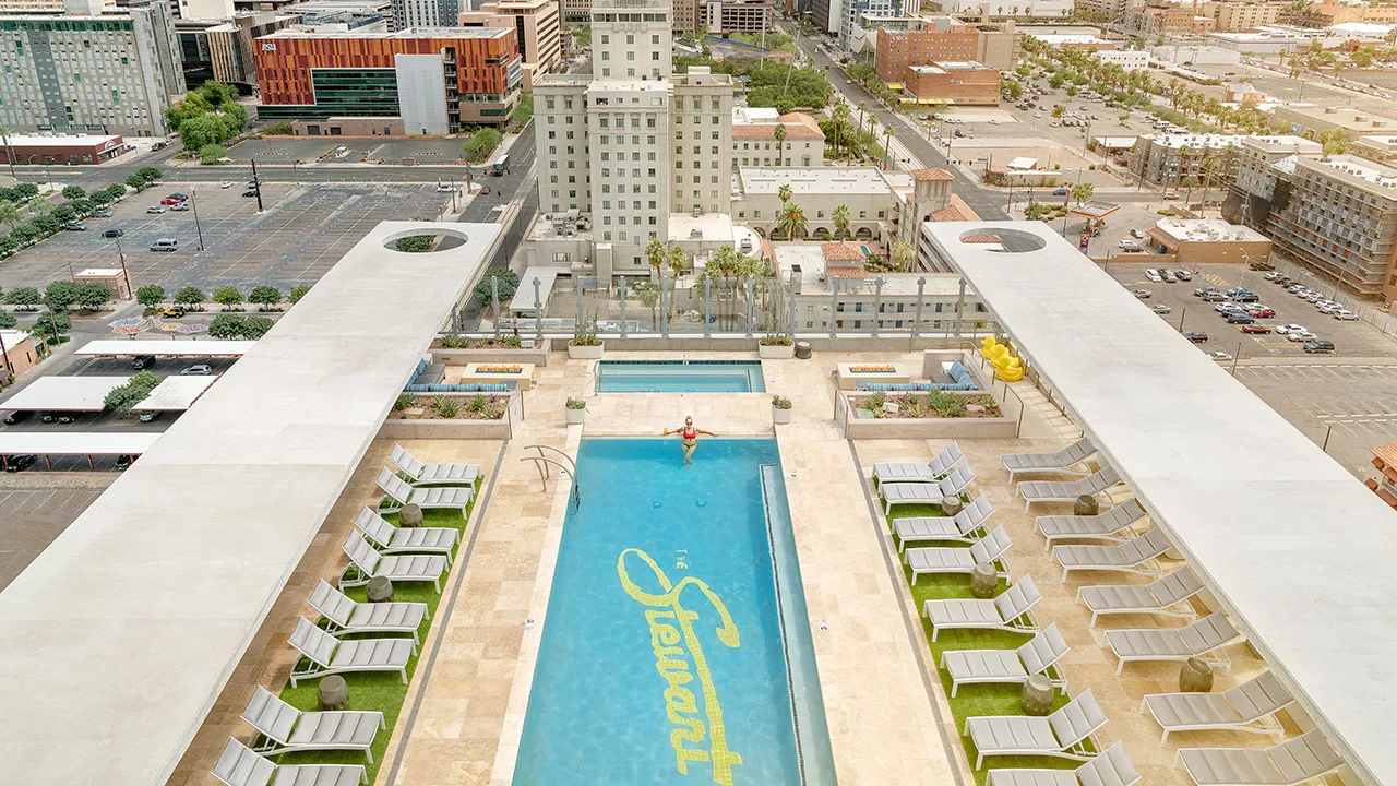 Rooftop pool with lounge chairs overlooking a city skyline in the distance.