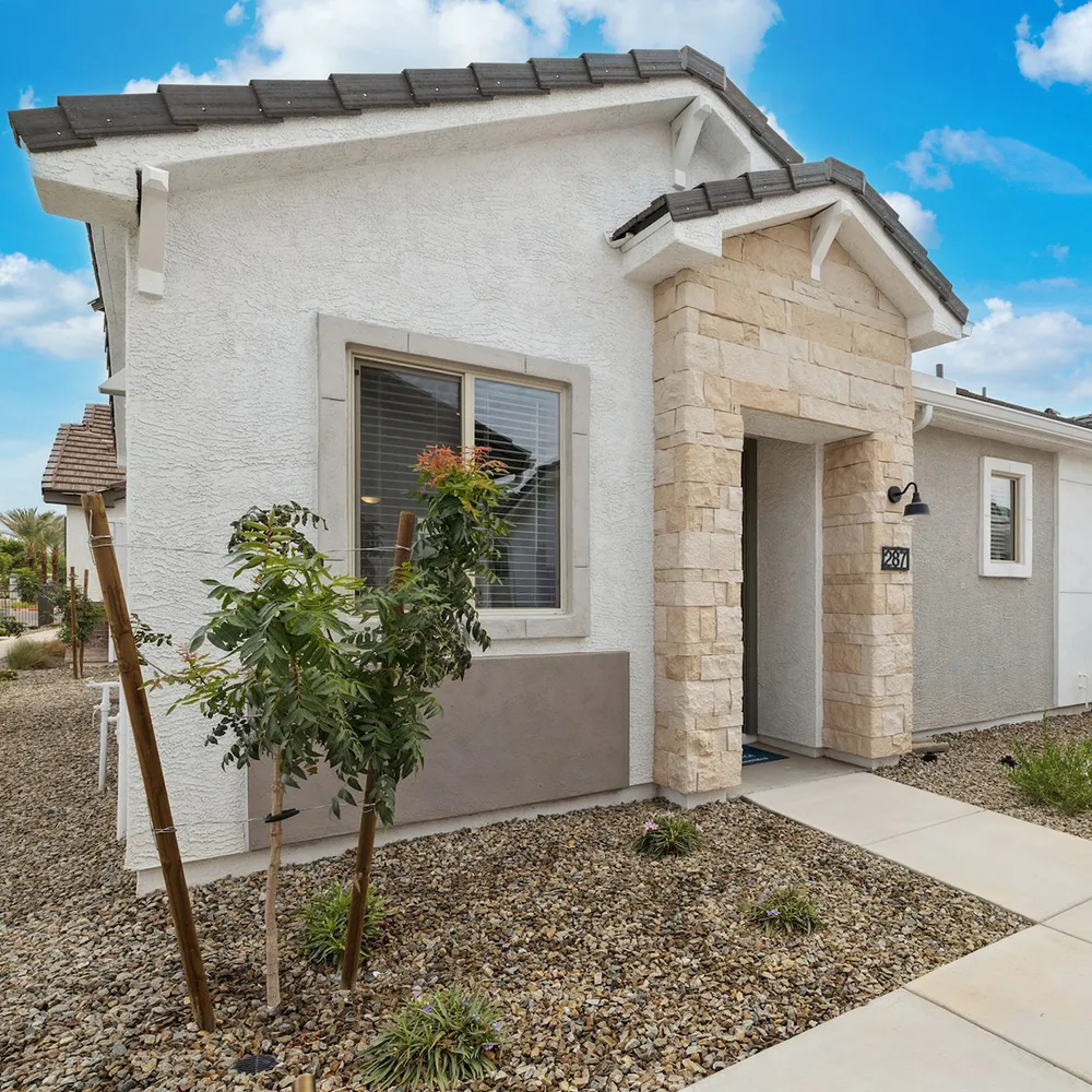 Modern single-story house exterior with stone entrance, gravel landscaping, and clear blue sky.