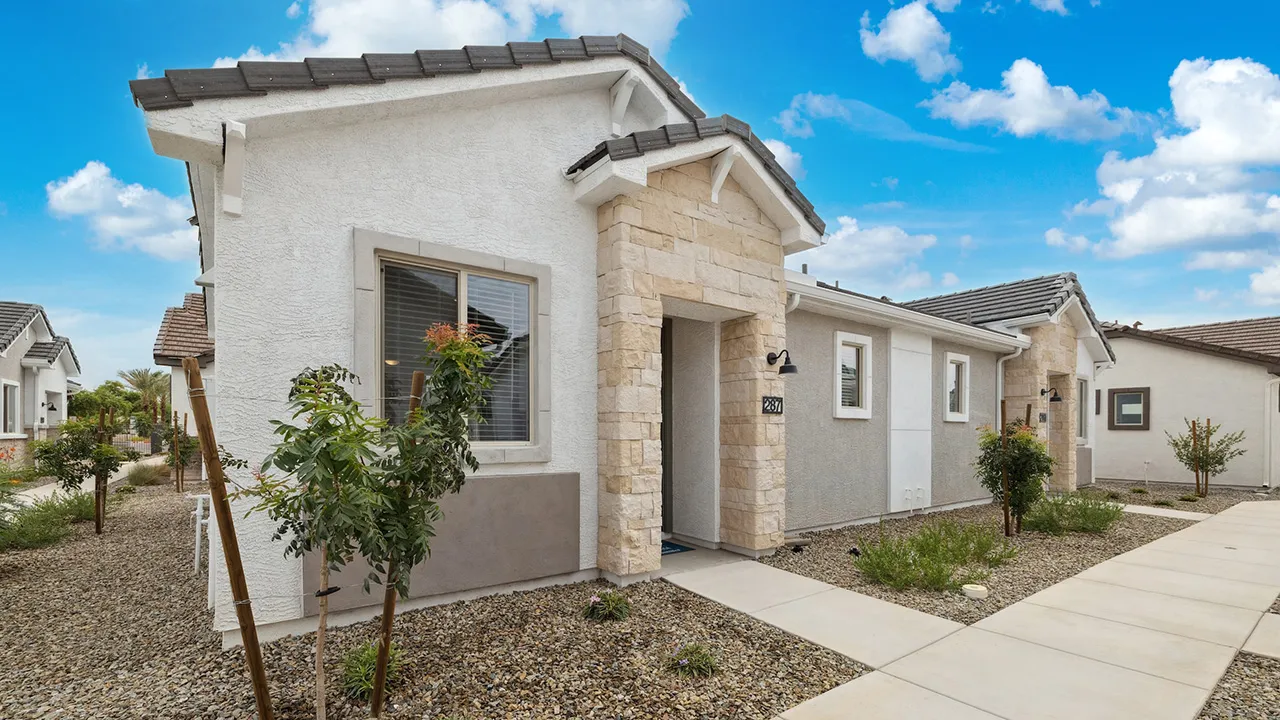 Modern single-story house exterior with stone entrance, gravel landscaping, and clear blue sky.