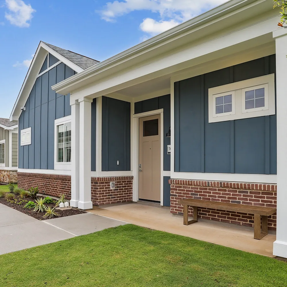 Exterior of a modern blue and brick house with white accents, front door, and a wooden bench on porch.