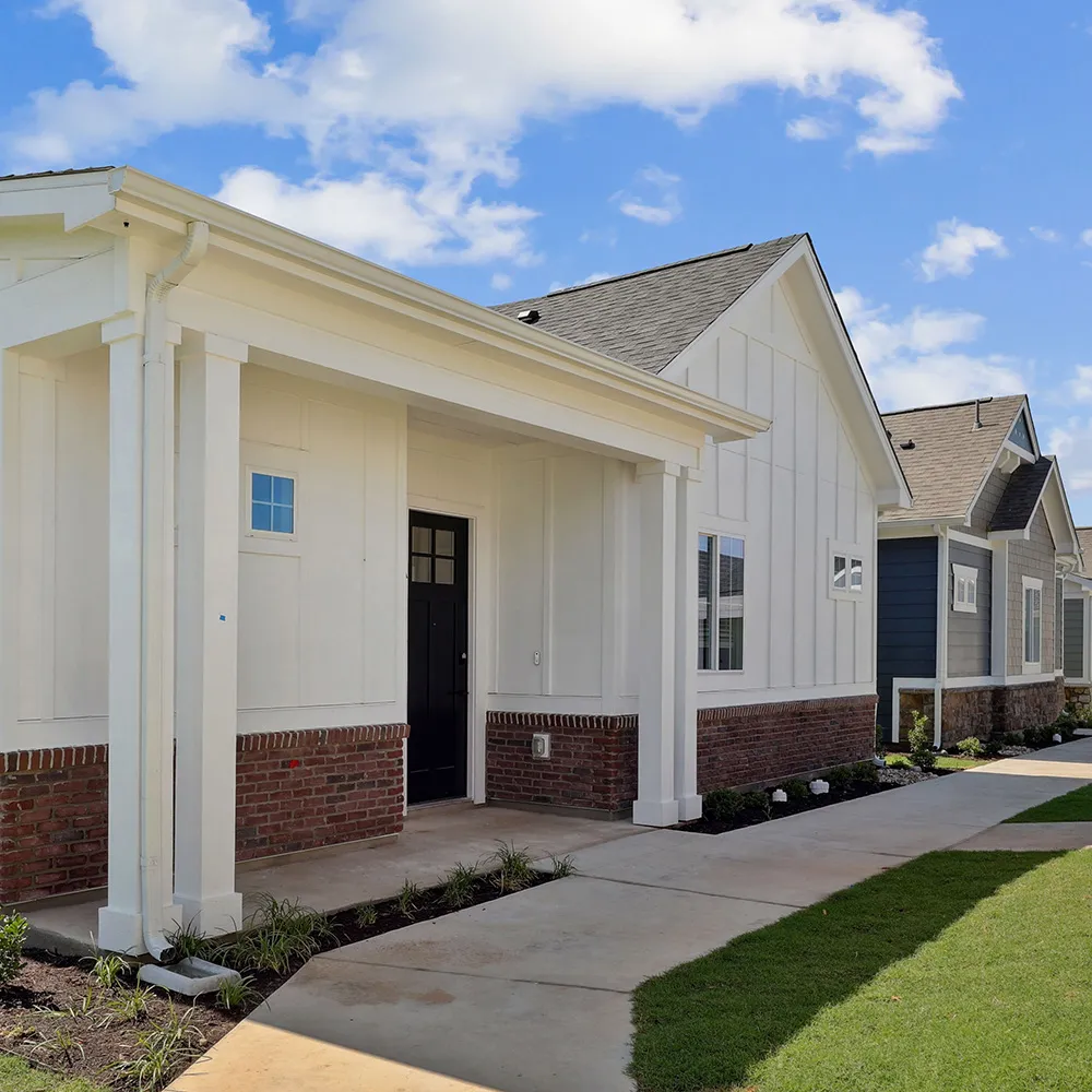 White house exterior with brick accents, black front door, and a concrete walkway leading to it.