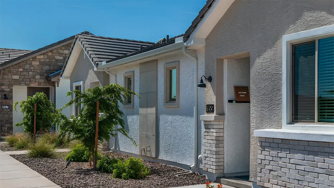 Exterior view of residential homes with stucco walls, stone accents, landscaping, and clear blue sky.