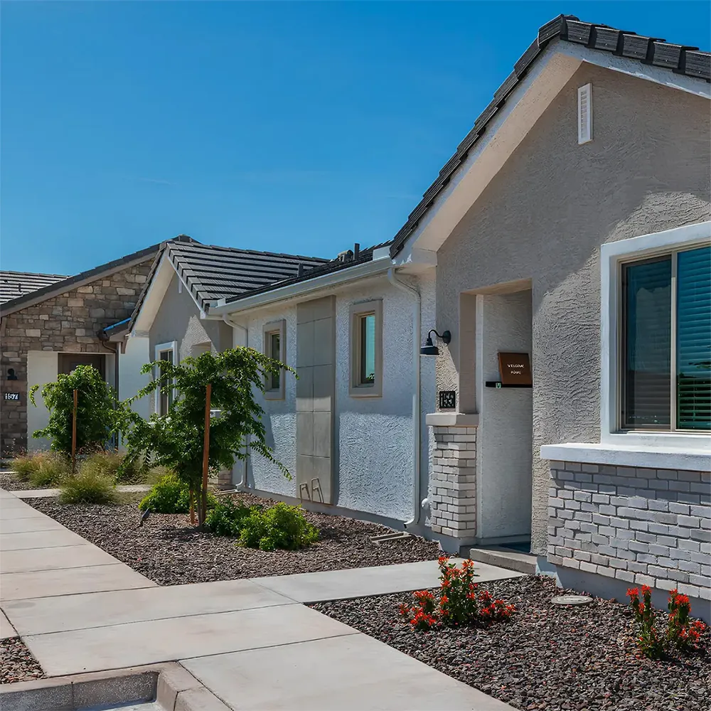 Exterior view of residential homes with stucco walls, stone accents, landscaping, and clear blue sky.