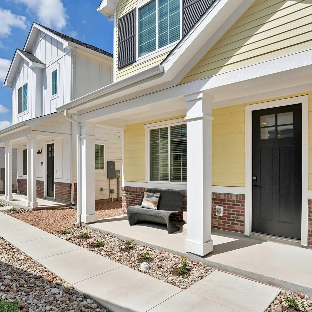 Exterior of two-story homes with white and yellow siding, black doors, and a stone and brick facade.