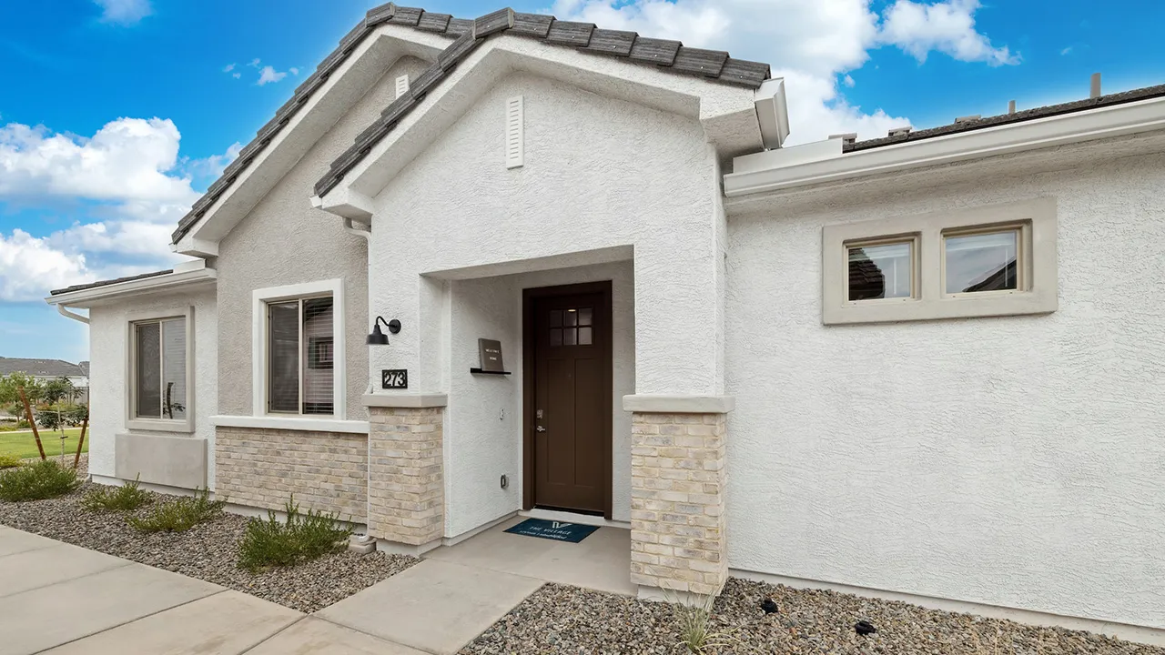 Modern beige house exterior with brown front door, stone accents, and blue welcome mat under porch roof.