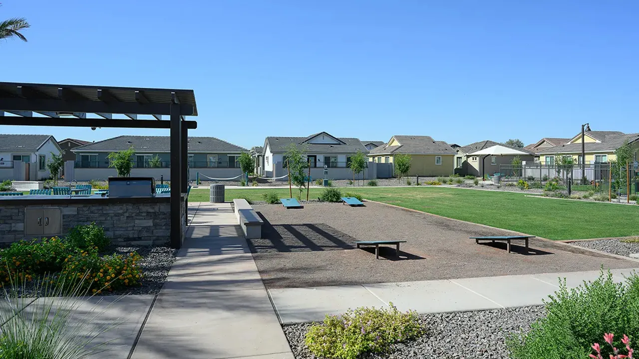 Community park with a hammock, swing bench, palm trees, grassy lawn, and houses in the background.