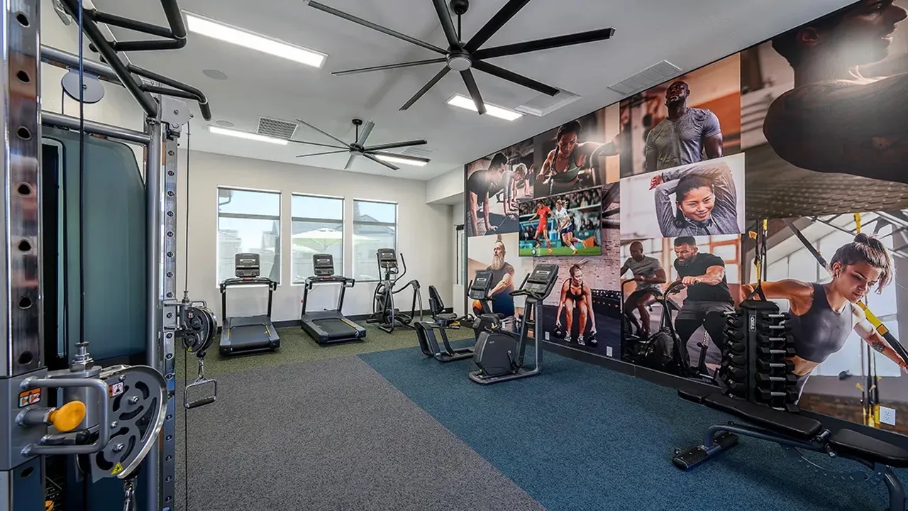 Gym room with treadmills, exercise bikes, wall with fitness photos, and ceiling fans.