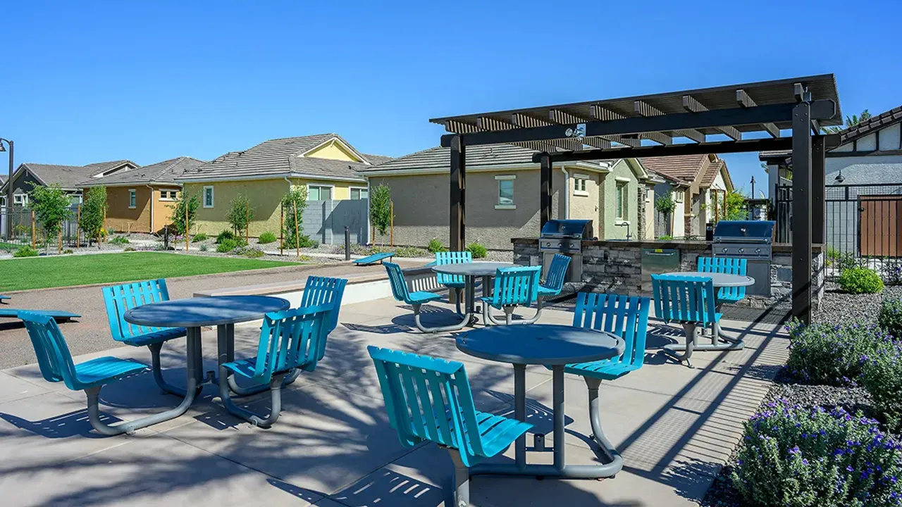 Outdoor patio area with blue chairs, tables, and two stainless steel grills under a pergola.