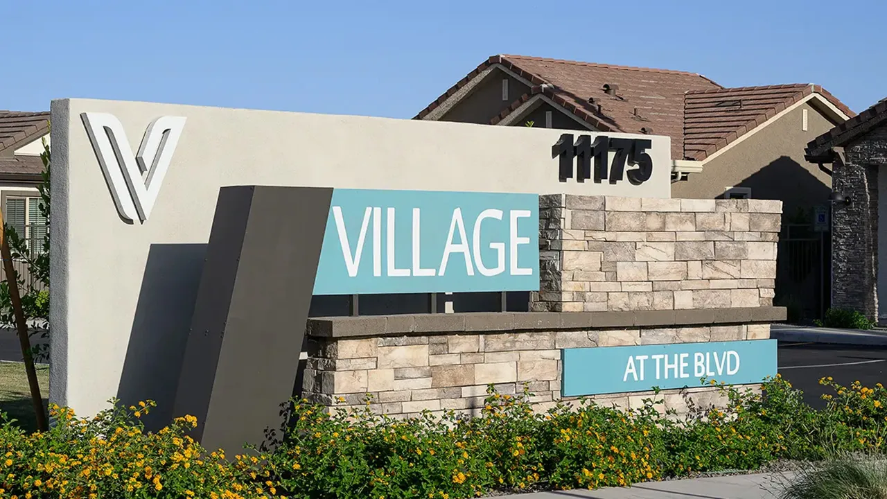 Stone entrance sign reading 'VILLAGE AT THE BLVD' with address number 11175 and houses in background.