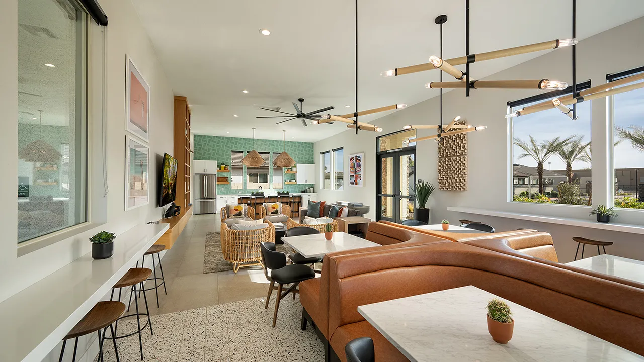 Modern clubhouse seating area with marble tables, leather booths, wicker chairs, and a stylish kitchen in background.