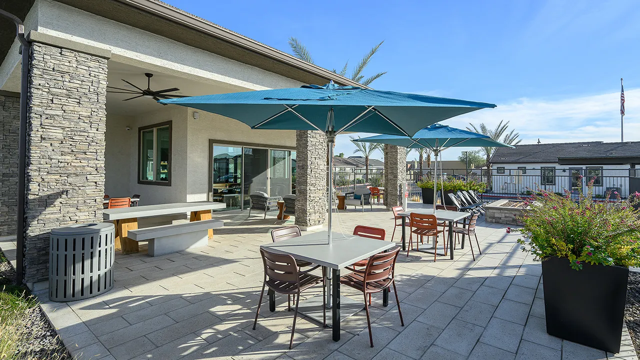 Outdoor patio with tables, blue umbrellas, chairs, lounge seating, and potted plants under blue sky.