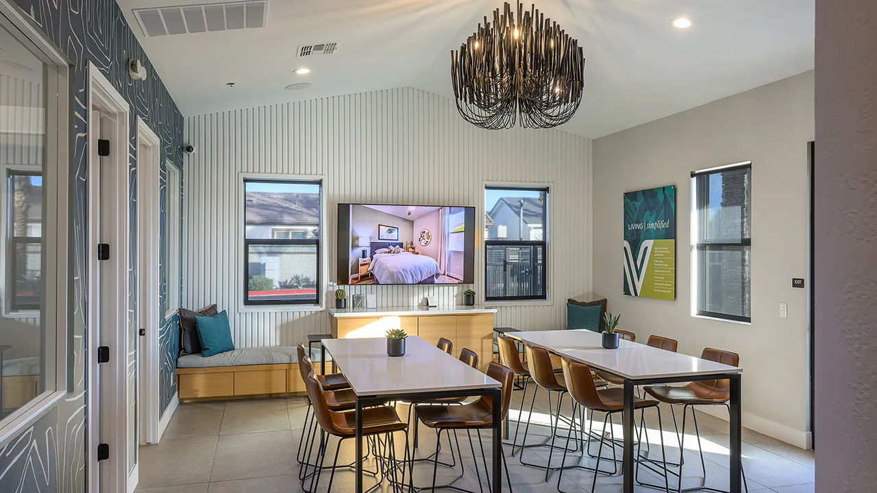 leasing office with white tables, brown chairs, a TV on a striped wall, and a black chandelier.