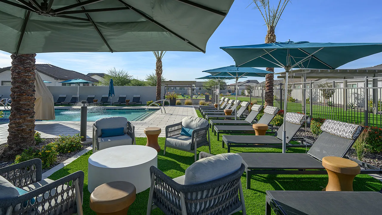 Outdoor poolside seating area with wicker chairs, umbrellas, and loungers on artificial grass.
