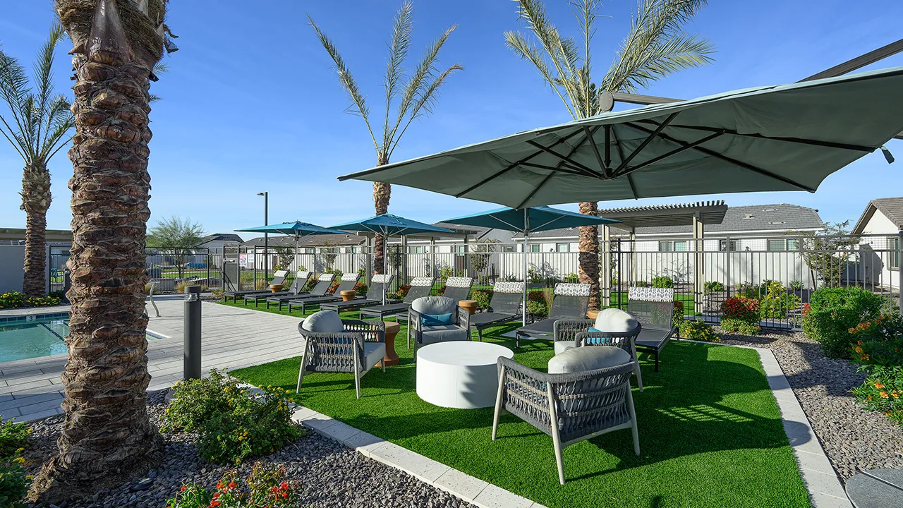Outdoor poolside seating area with wicker chairs, umbrellas, and loungers on artificial grass.
