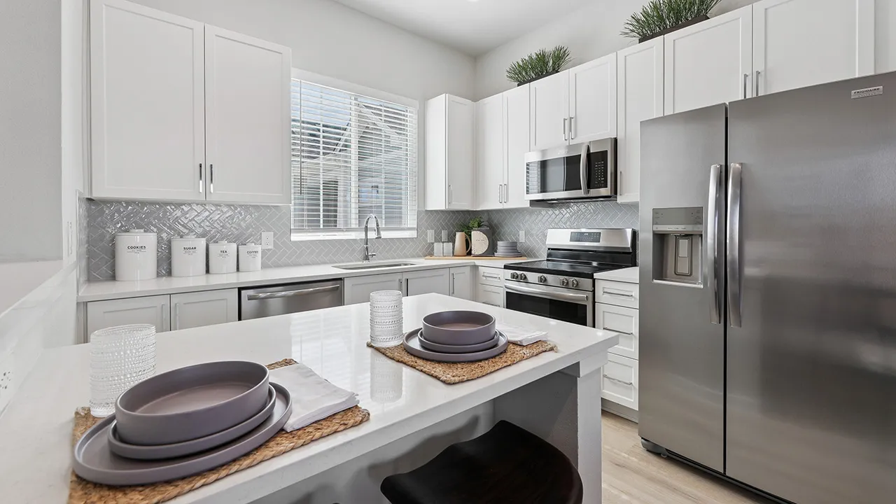 Modern kitchen with white cabinets, stainless steel appliances, gray tile backsplash, and island.