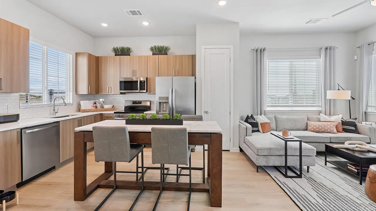 Modern kitchen with wooden cabinets and island opens to living room with gray sectional sofa and coffee table.