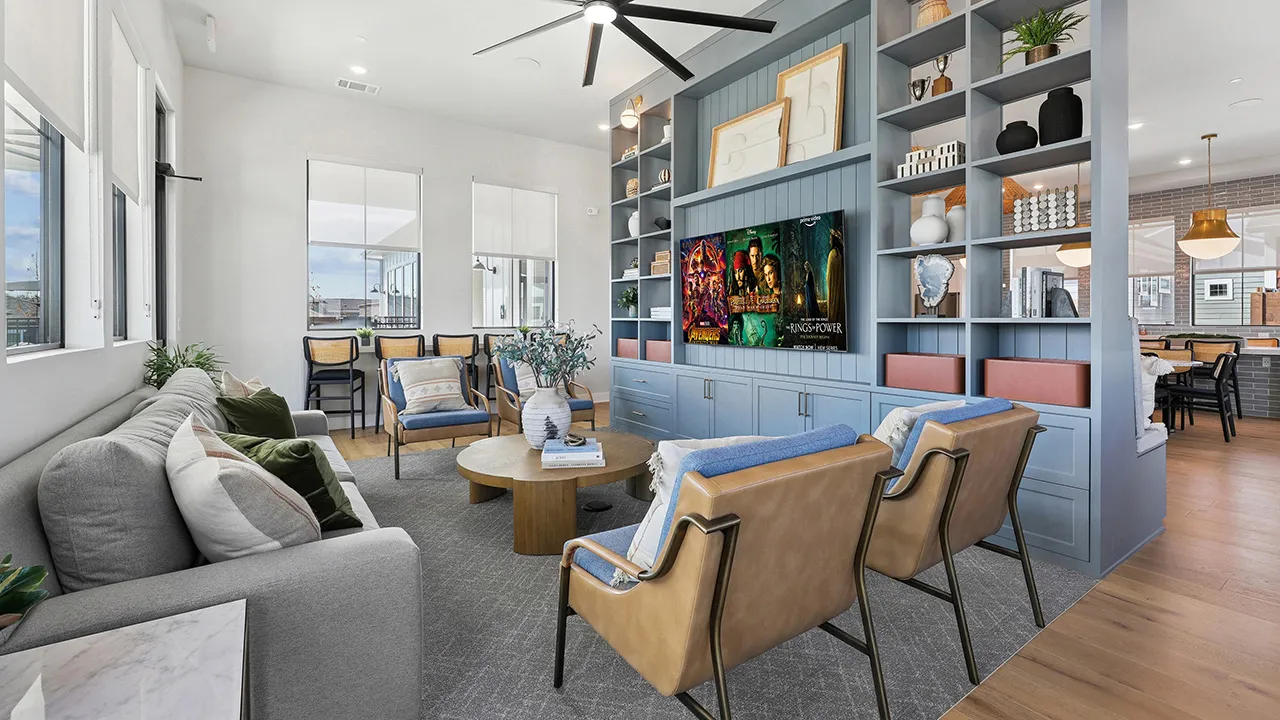 Modern clubhouse with blue built-in shelves, TV, gray sofa, leather chairs, and round wooden coffee table.