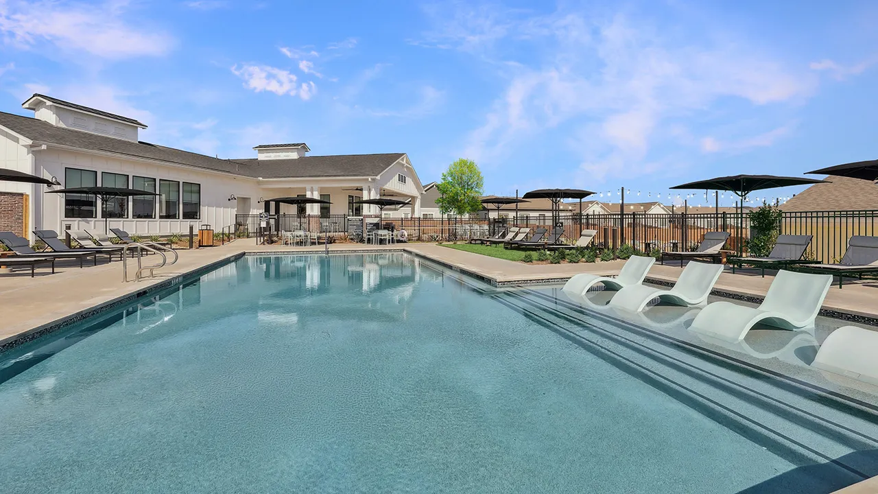 Outdoor swimming pool with lounge chairs, umbrellas, and a building under a blue sky.