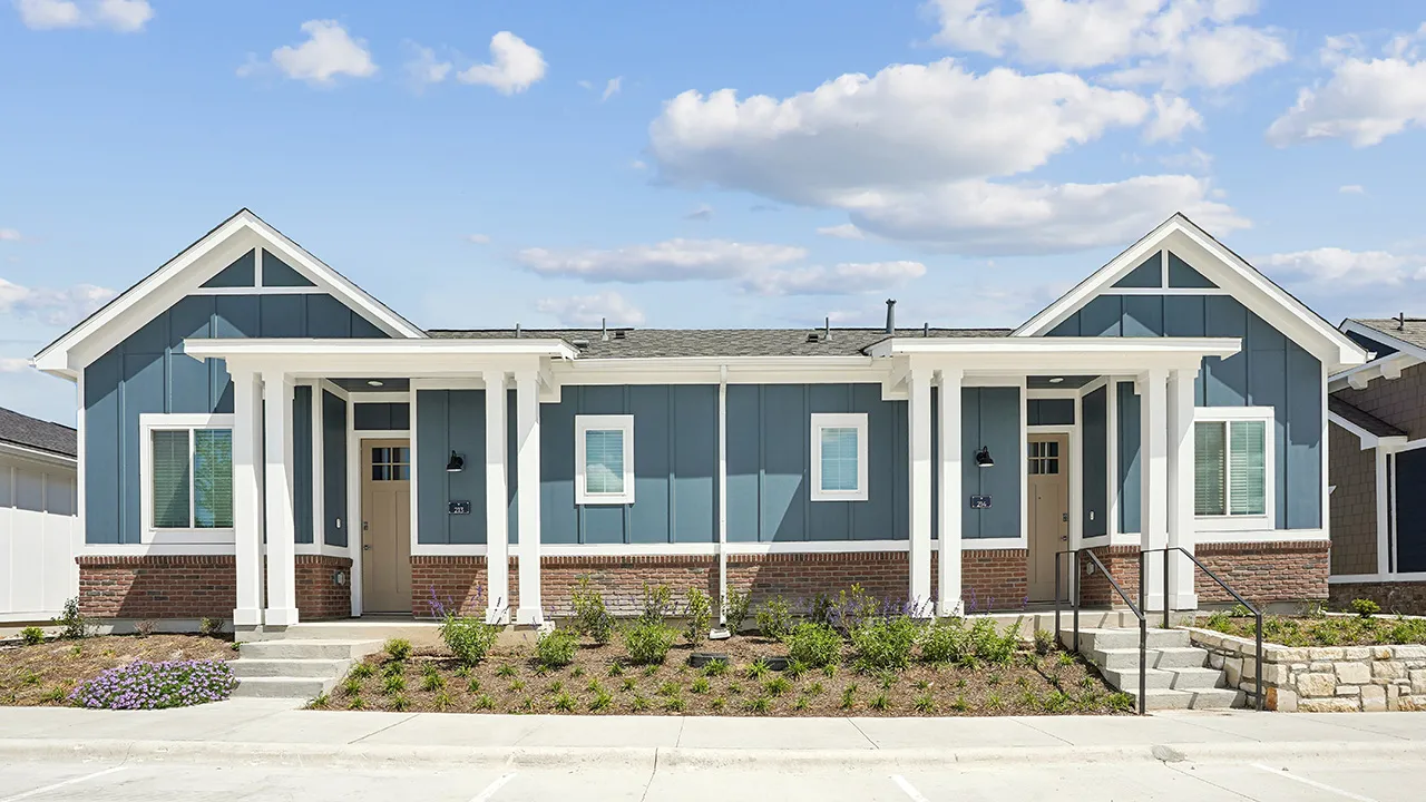 Single-story duplex with brick base, blue siding, white trim, and a small front porch.