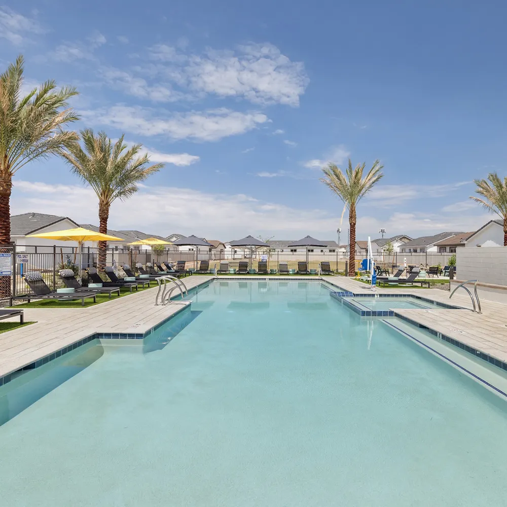 Outdoor pool area with lounge chairs, yellow umbrellas, palm trees, and blue sky.