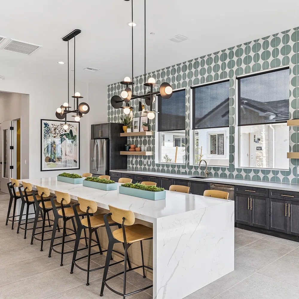 Modern kitchen with a long white marble island, wood chairs, pendant lights, and patterned wall tiles.