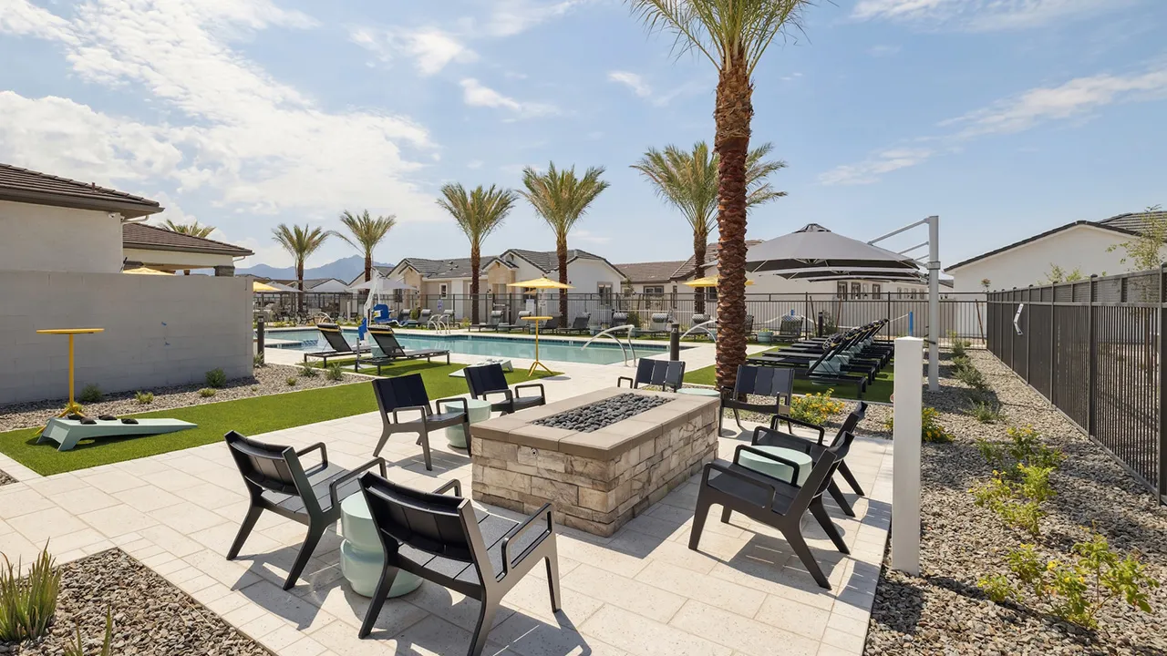 Outdoor lounge area with chairs, stone fire pit, palm trees, and blue sky in a residential neighborhood.