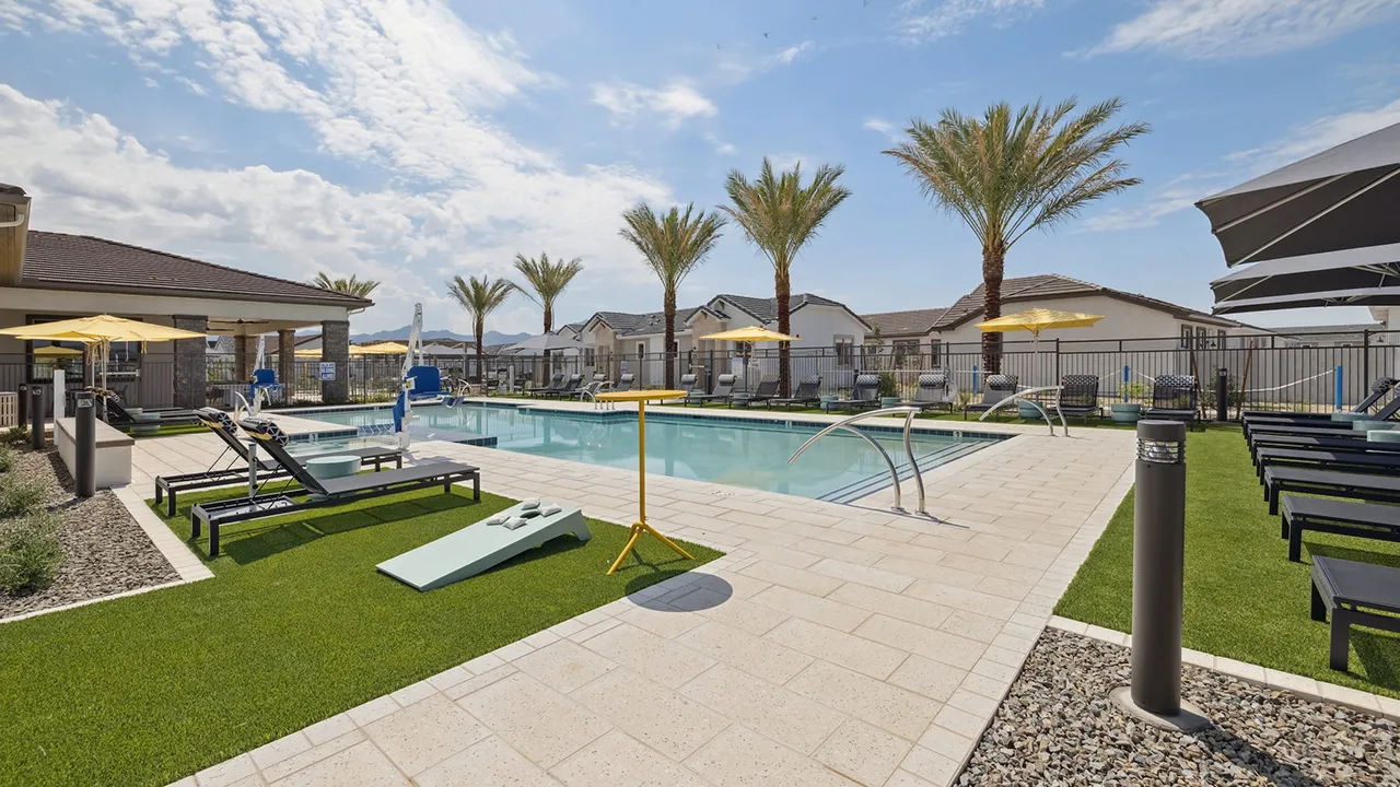 Outdoor pool area with lounge chairs, yellow umbrellas, cornhole, palm trees, and blue sky.