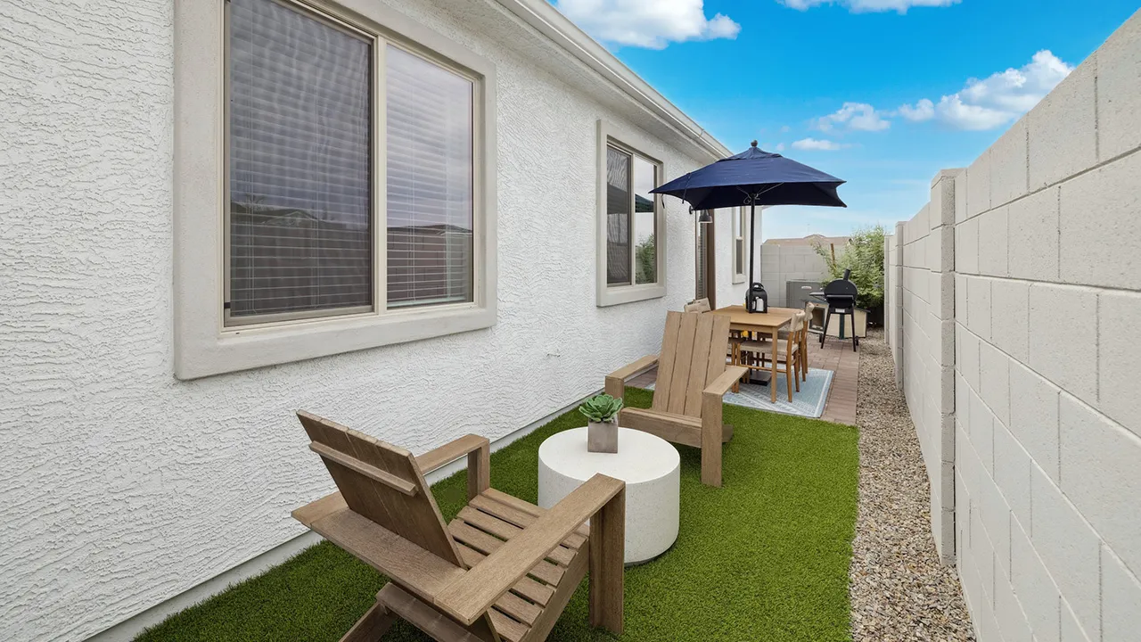 Outdoor patio with two wooden chairs, a round table, dining set with umbrella, and a grill by a white house.