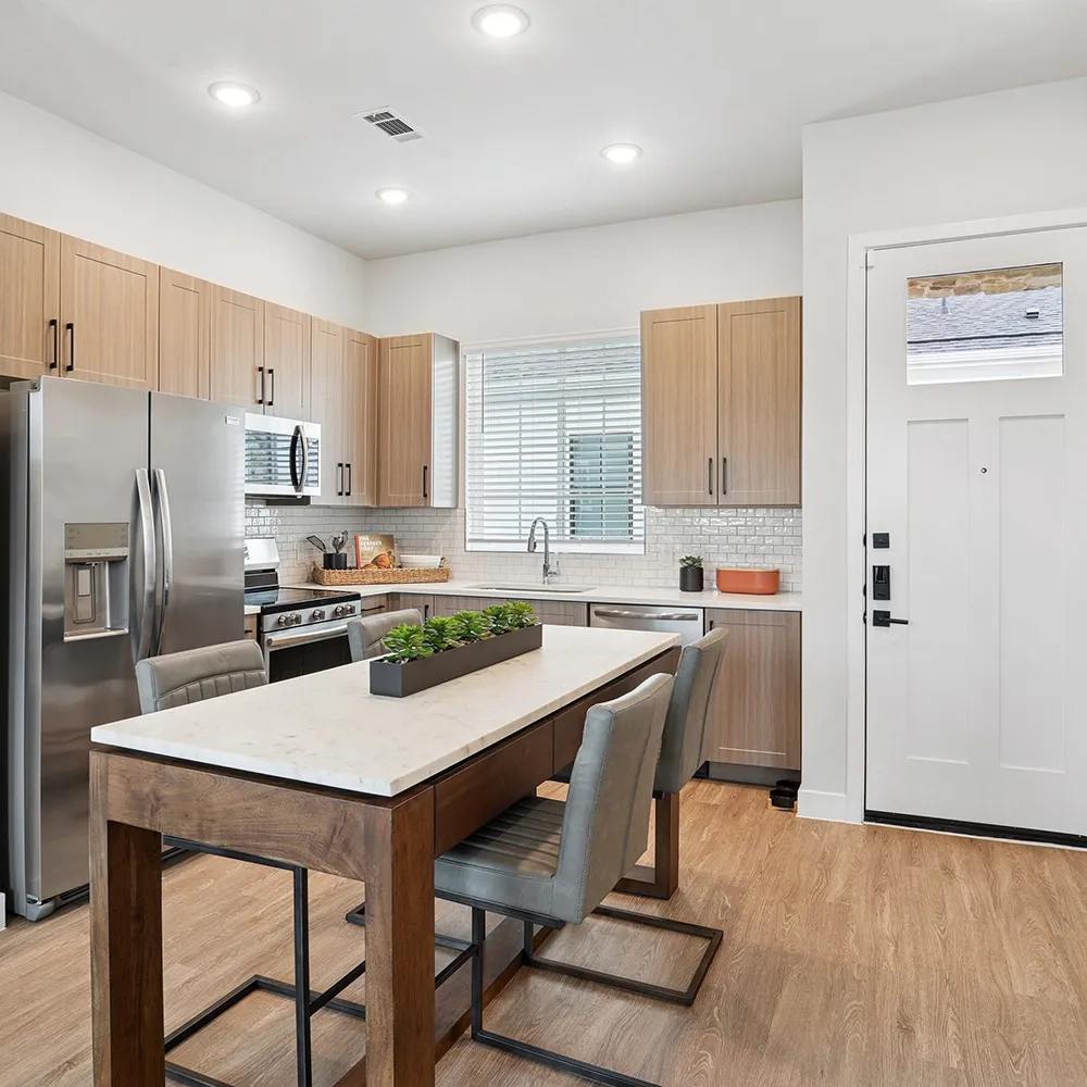 Modern kitchen with wood-look cabinets, stainless steel fridge, large window over sink, and island.