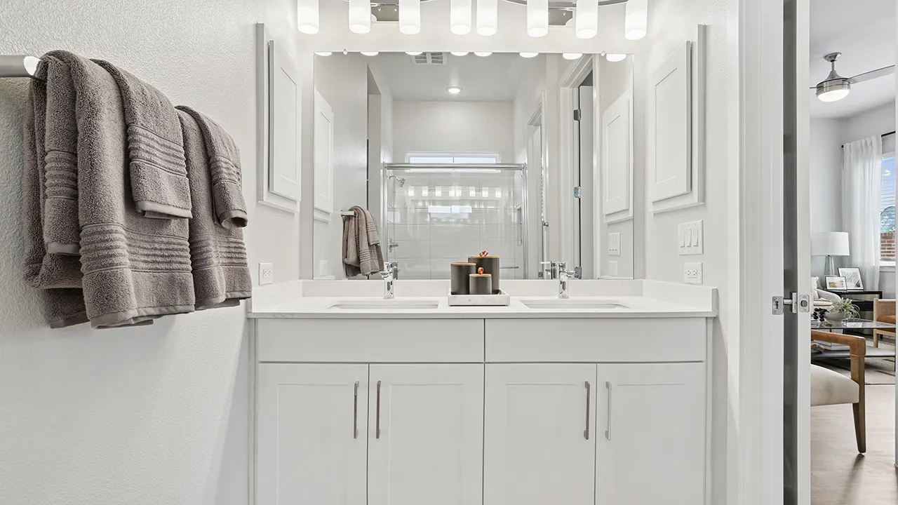 Modern bathroom with white vanity, large mirror, and gray towels hung on a rack.