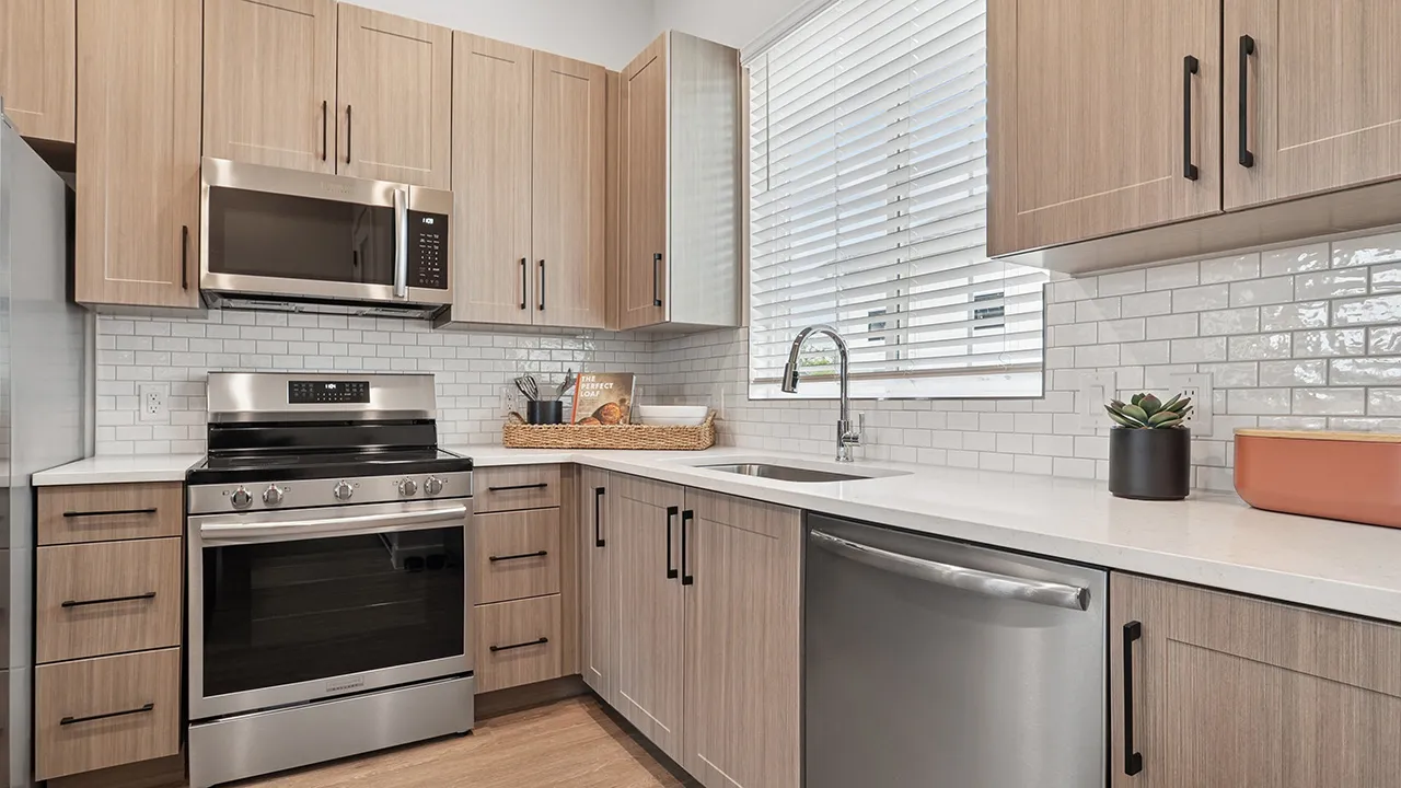 Modern kitchen with wood-look cabinets, stainless steel stove and dishwasher, large window over sink.