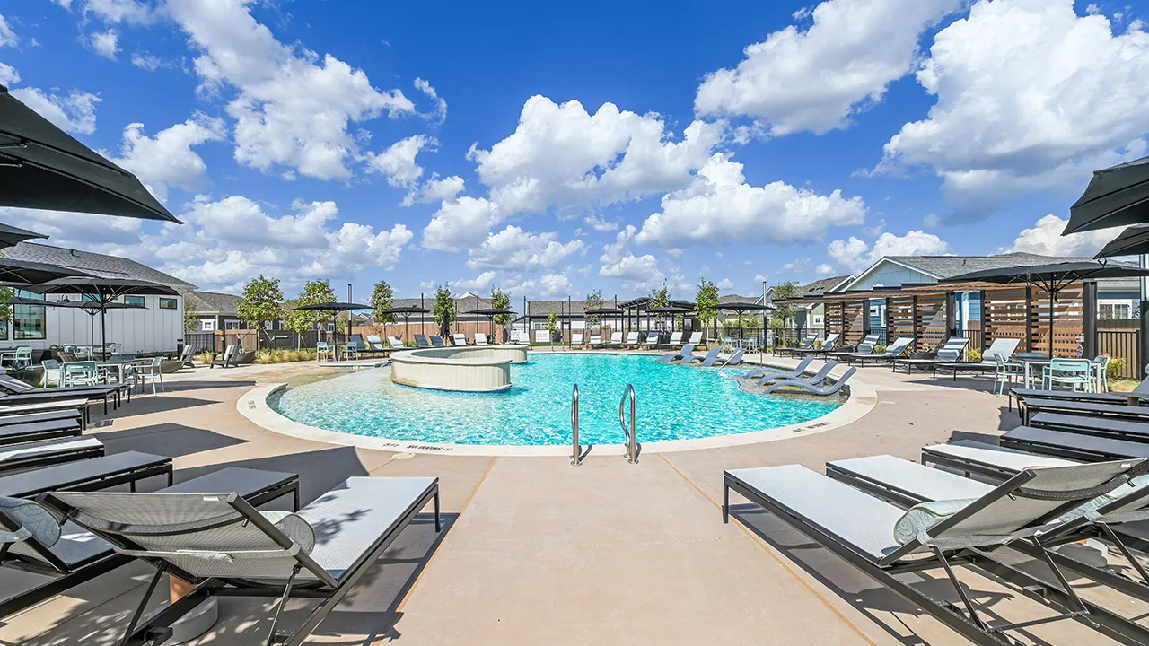 Clear blue swimming pool with lounge chairs and umbrellas under a partly cloudy sky.