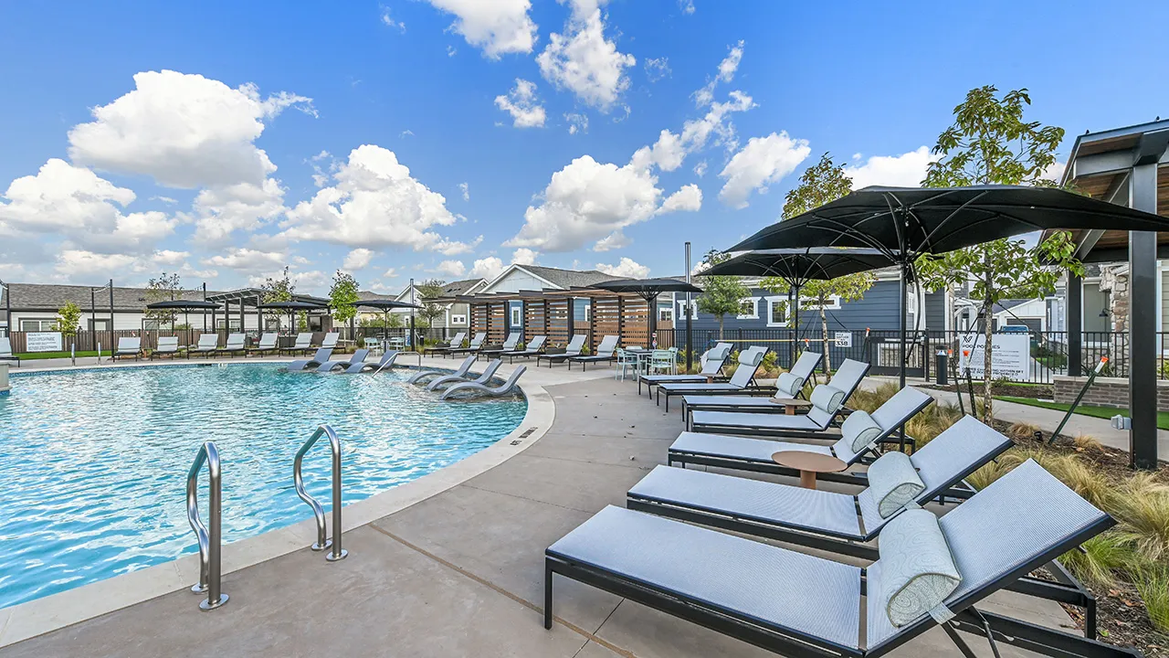 Clear blue swimming pool with lounge chairs and umbrellas under a partly cloudy sky.
