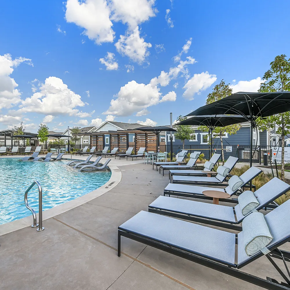 Clear blue swimming pool with lounge chairs and umbrellas under a partly cloudy sky.