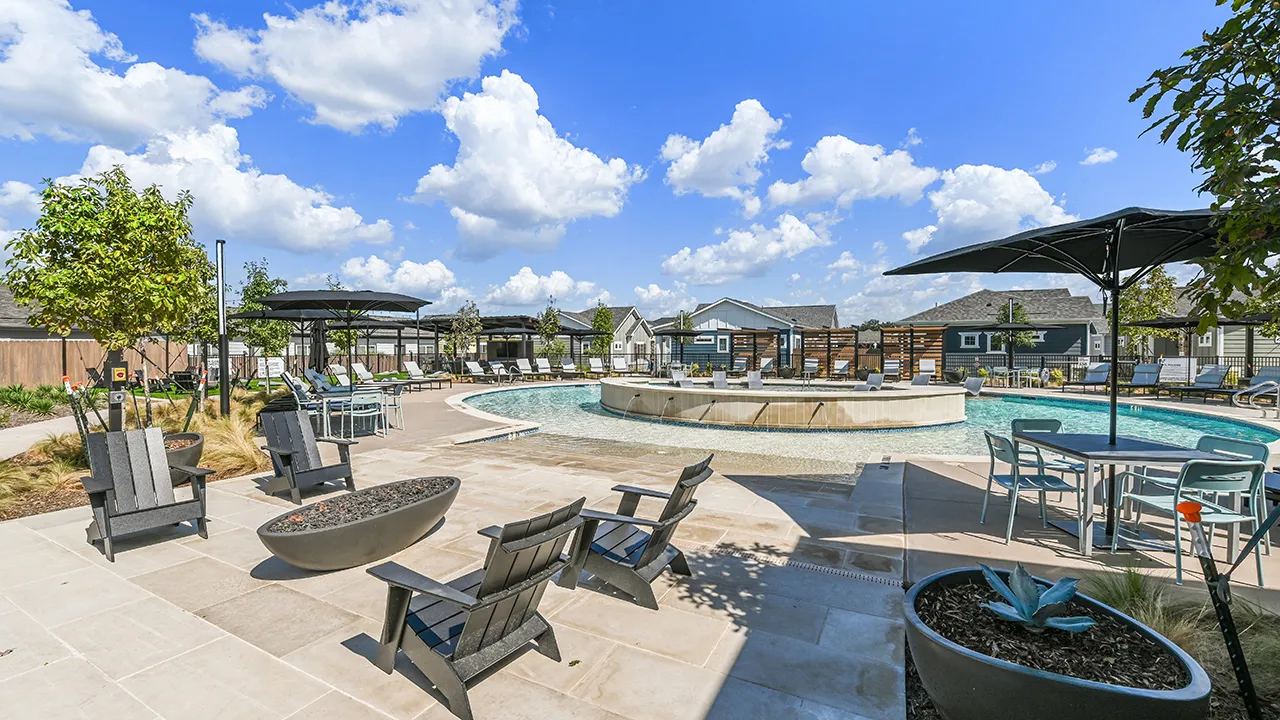 Clear blue swimming pool with lounge chairs, firepit, and umbrellas under a partly cloudy sky.
