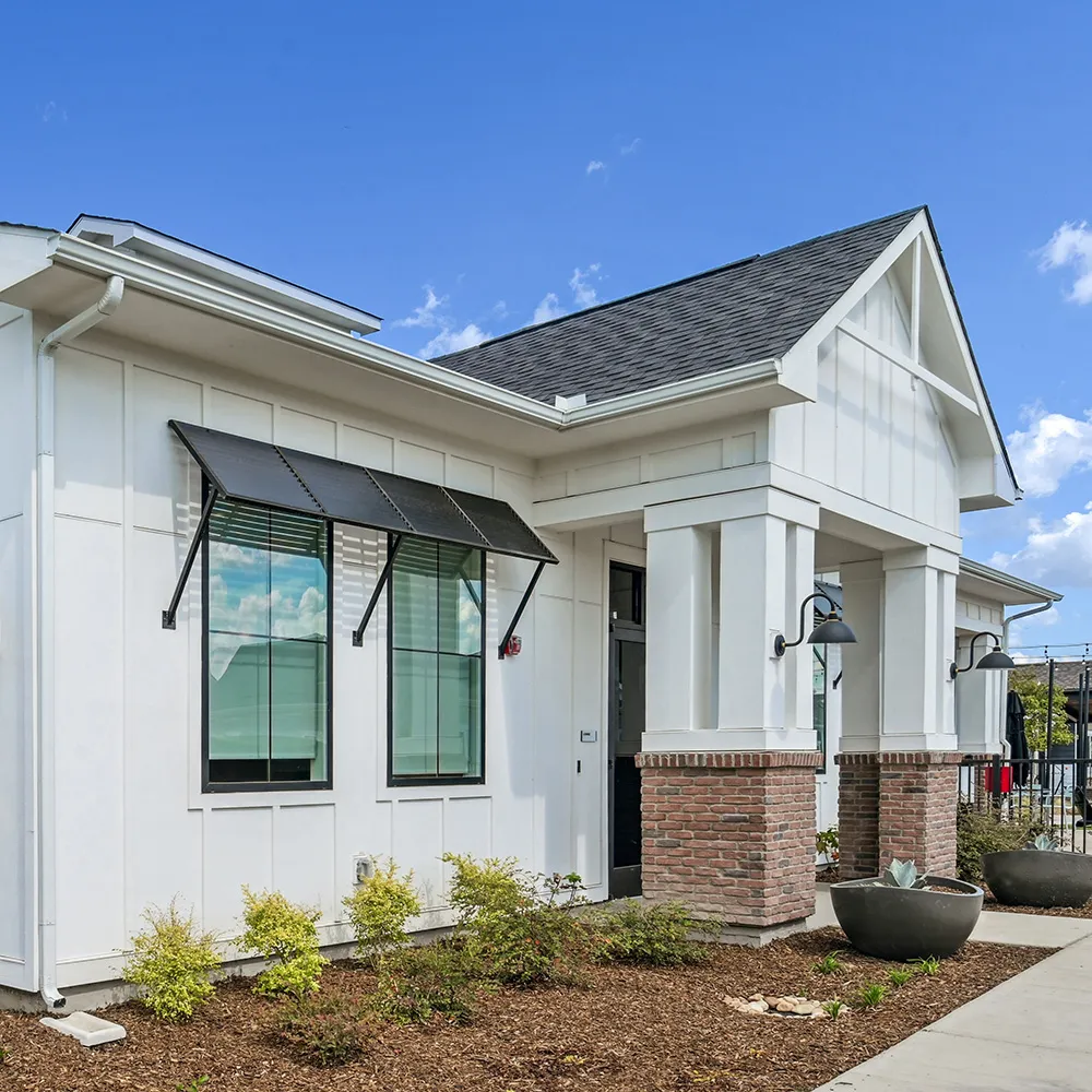 Exterior of a modern white and brick house with window shades and landscaping.