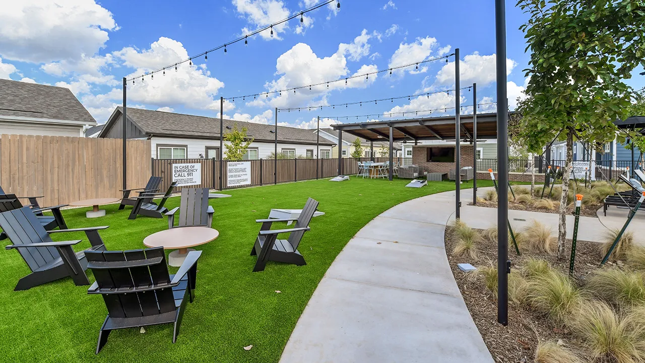 Outdoor seating area with black chairs, round tables, string lights, lawn games, and a covered patio.