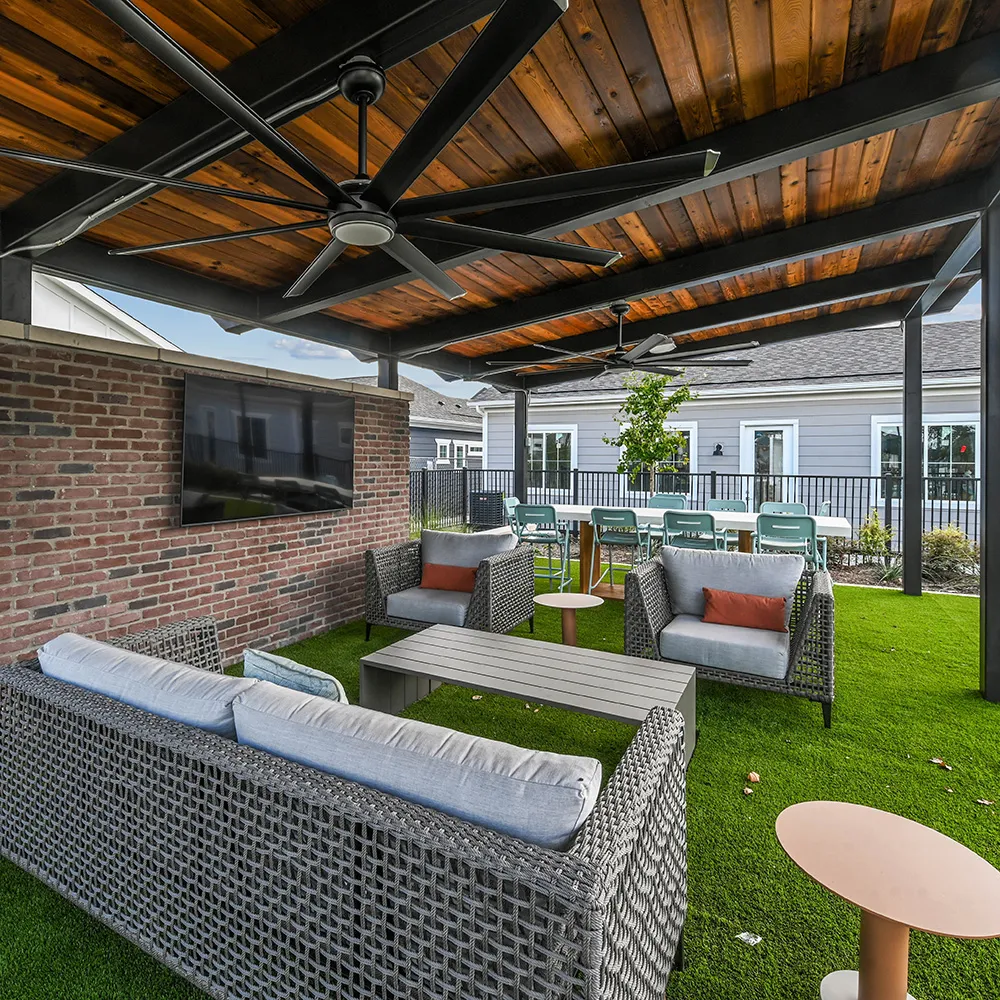 Outdoor seating area under a covered ramada with fan, coffee table, and mounted TV.